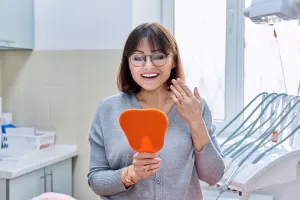 a smiling woman holding a hand mirror all on 4 implant placement seattle